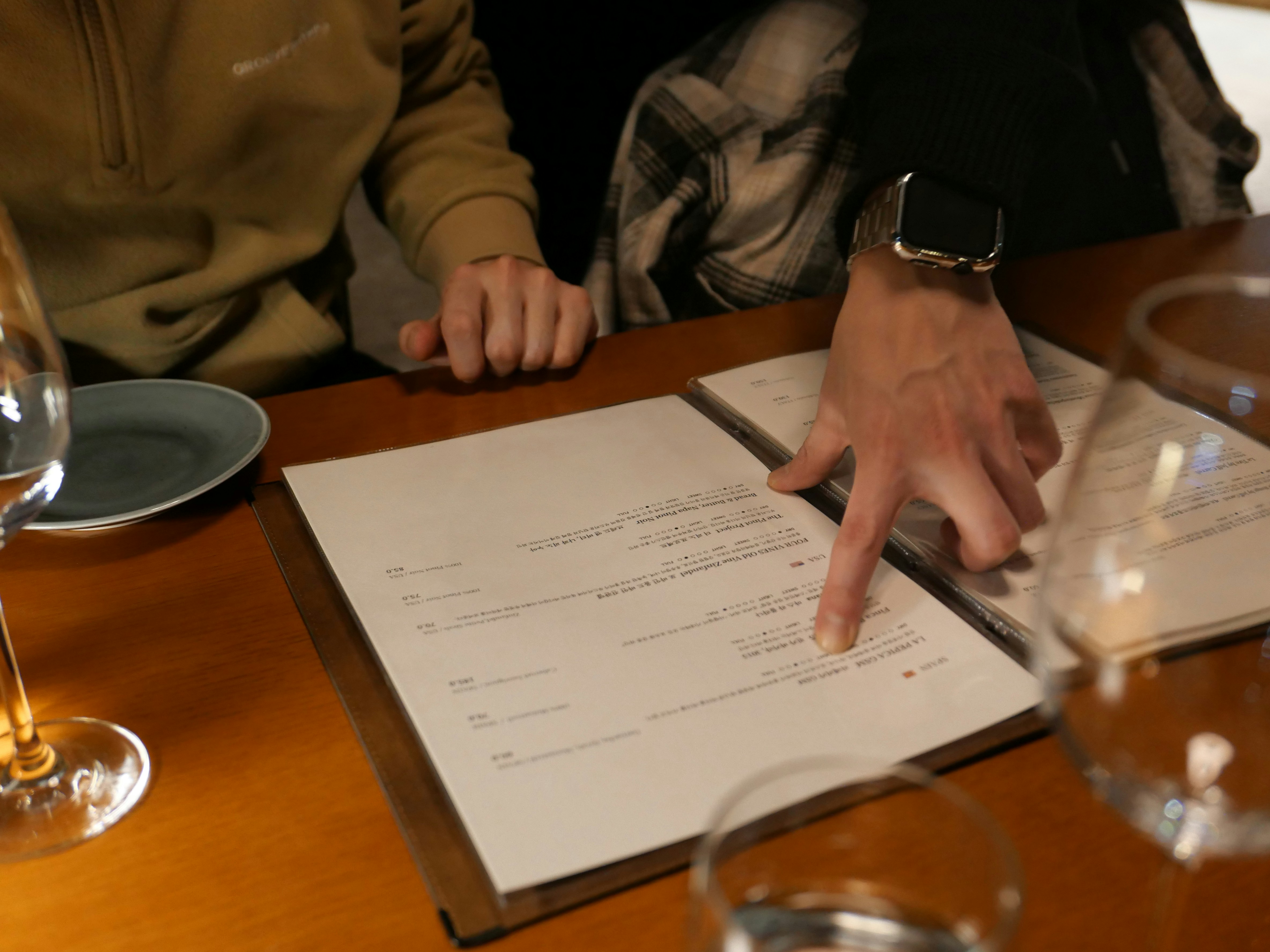 Two diners at a restaurant table reviewing a printed wine menu together.